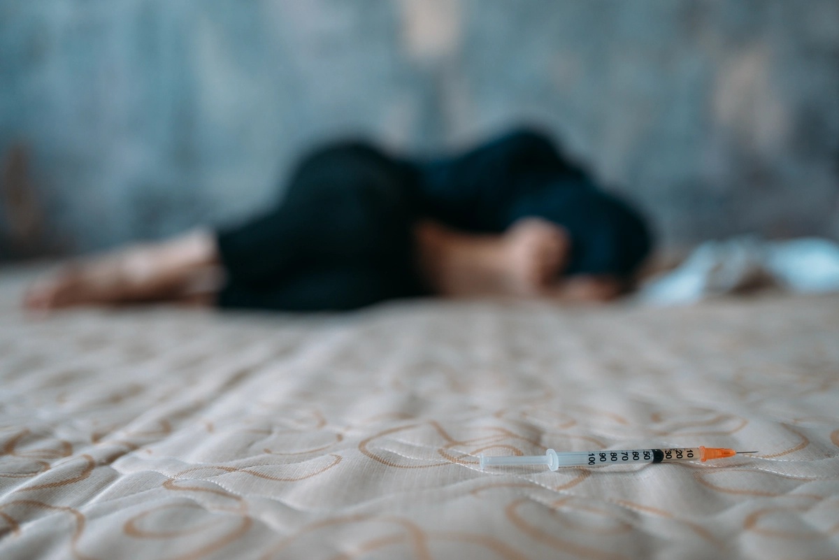 Fentanyl Addiction: Blurry picture of a man curled up with a needle in frame