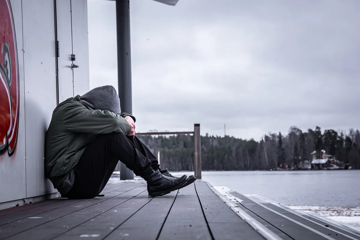 Man sitting in the rain with a coat suffering from Depression