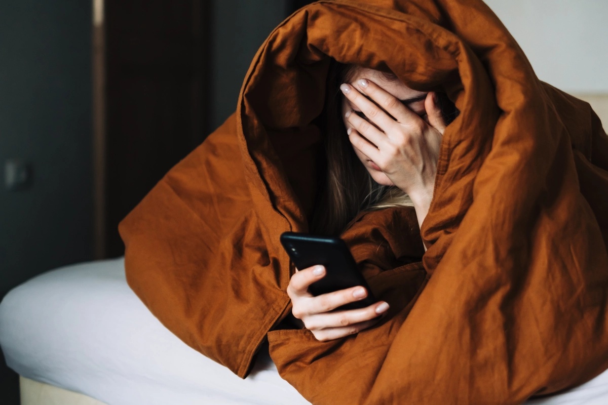 Phone Addiction: Woman looking at her phone wrapped in blankets