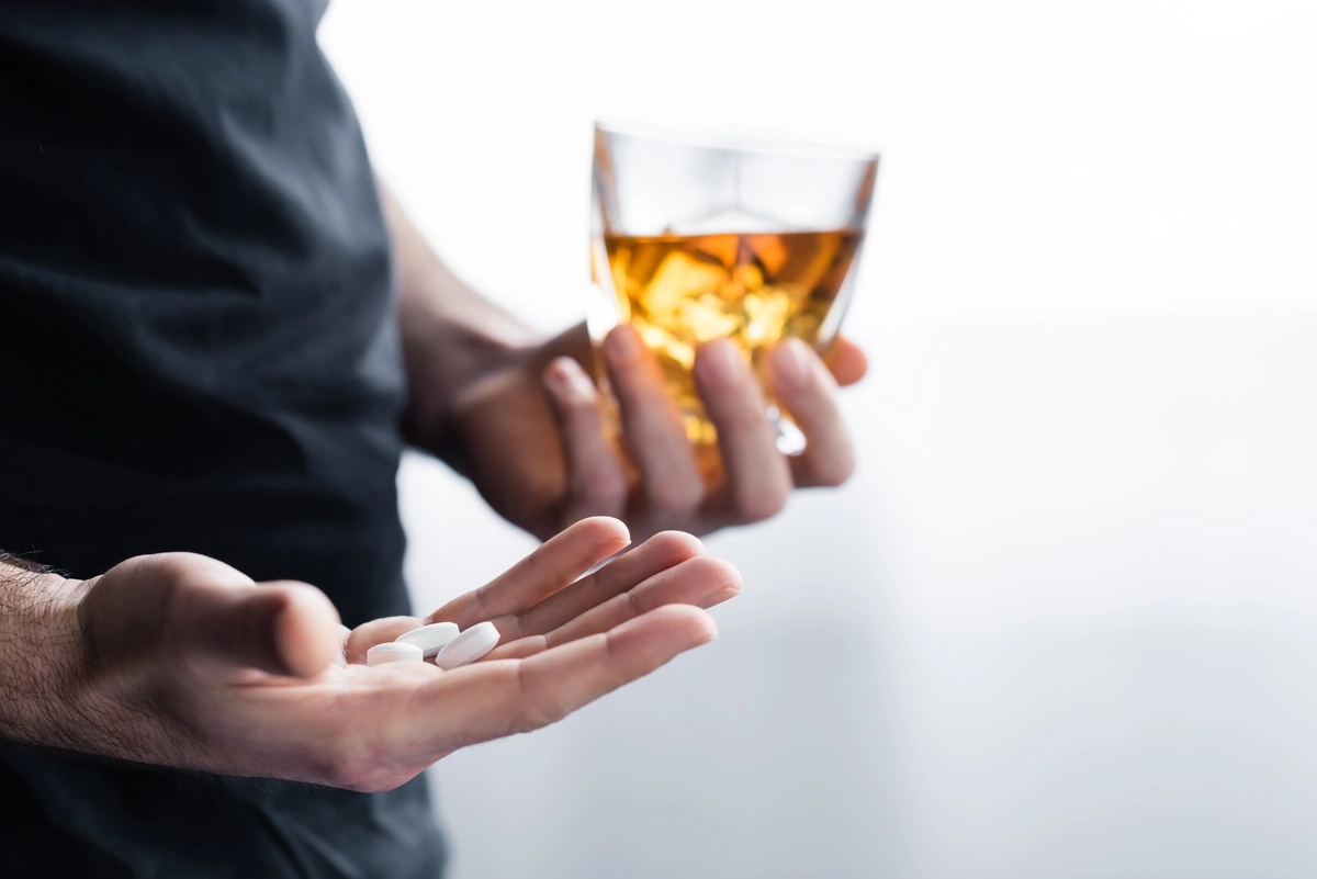 Stimulant Addiction: Man holding a glass of whiskey in one hand and pills in the other