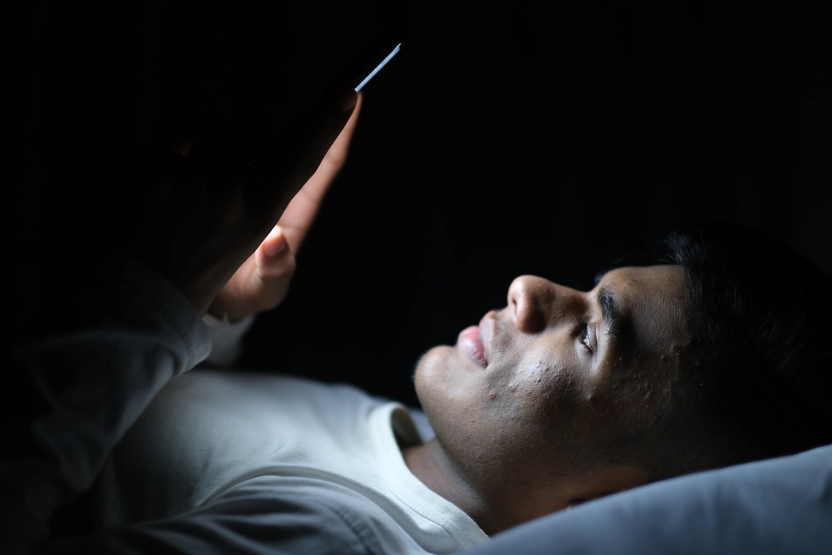 Phone Addiction: Man sitting in the dark staring at his phone
